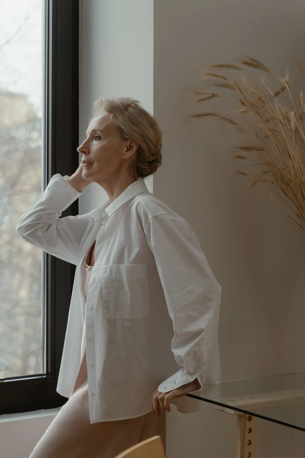 Woman in a white shirt standing in soft window light. Illustrative stock photograph, not a patient.