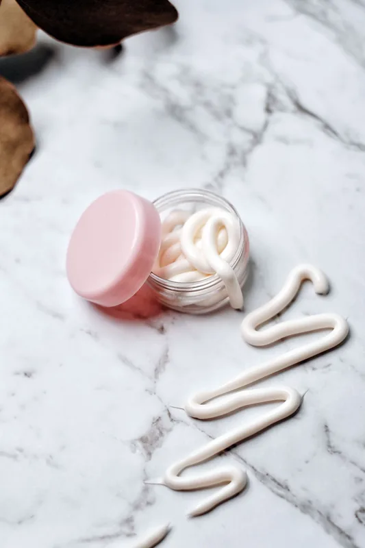 Ribbon of cream beside an open jar on marble. Illustrative stock photograph, not the product.