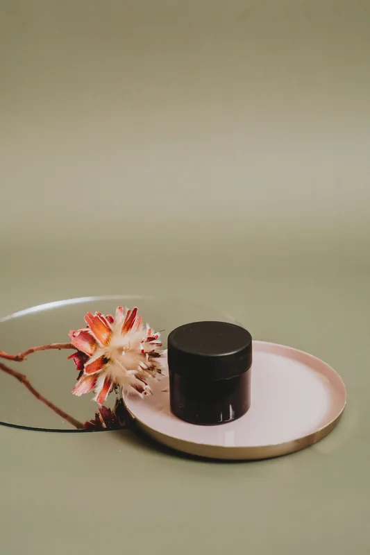 Dark jar on a tray with a dried flower. Illustrative stock photograph, not the product.