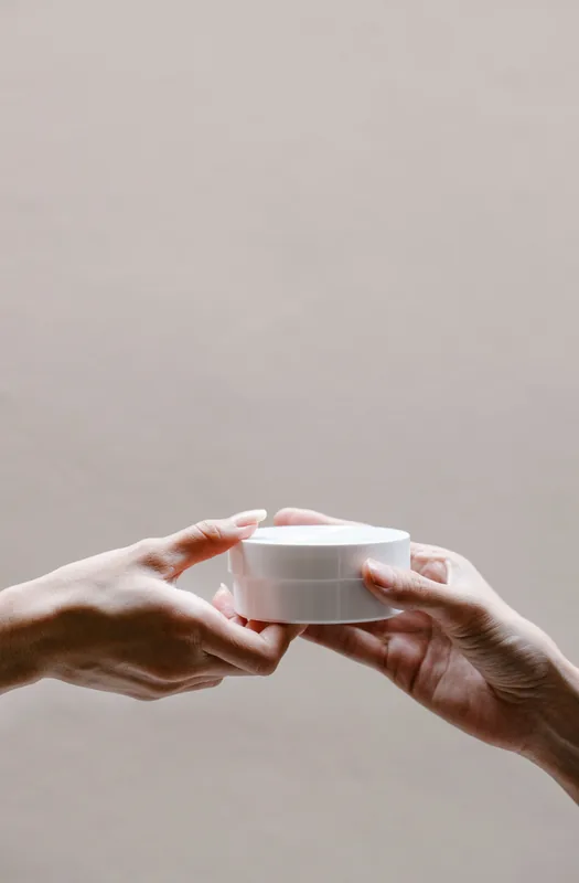 Hands offering a small white jar. Illustrative stock photograph, not the product.