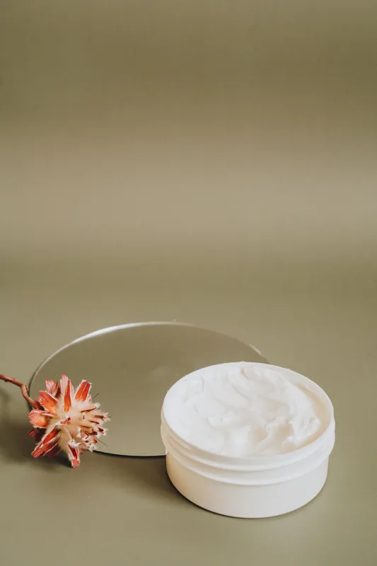 Open white jar of cream with a pink flower. Illustrative stock photograph, not the product.