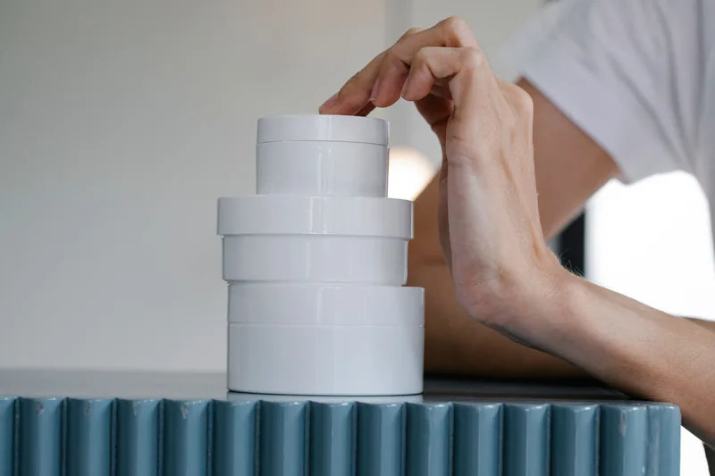 Hand resting on a stack of white jars. Illustrative stock photograph, not the product.