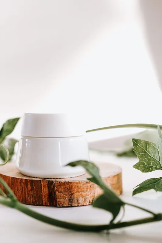 White jar on a wooden slice with green leaves. Illustrative stock photograph, not the product.