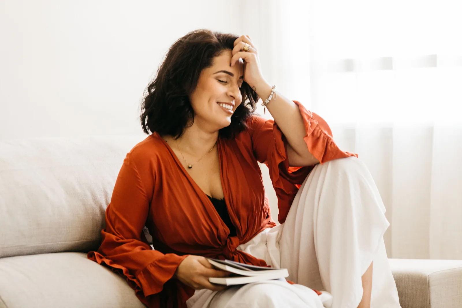 Woman laughing on her sofa with a book. Illustrative stock photograph, not a patient.